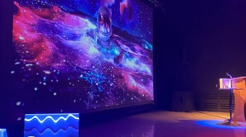 Purple and blue theater lights shine on 3D printed objects in the IMRC Center's Adaptive Presentation and Performance Environment. An astronaut floats on the projection screen.