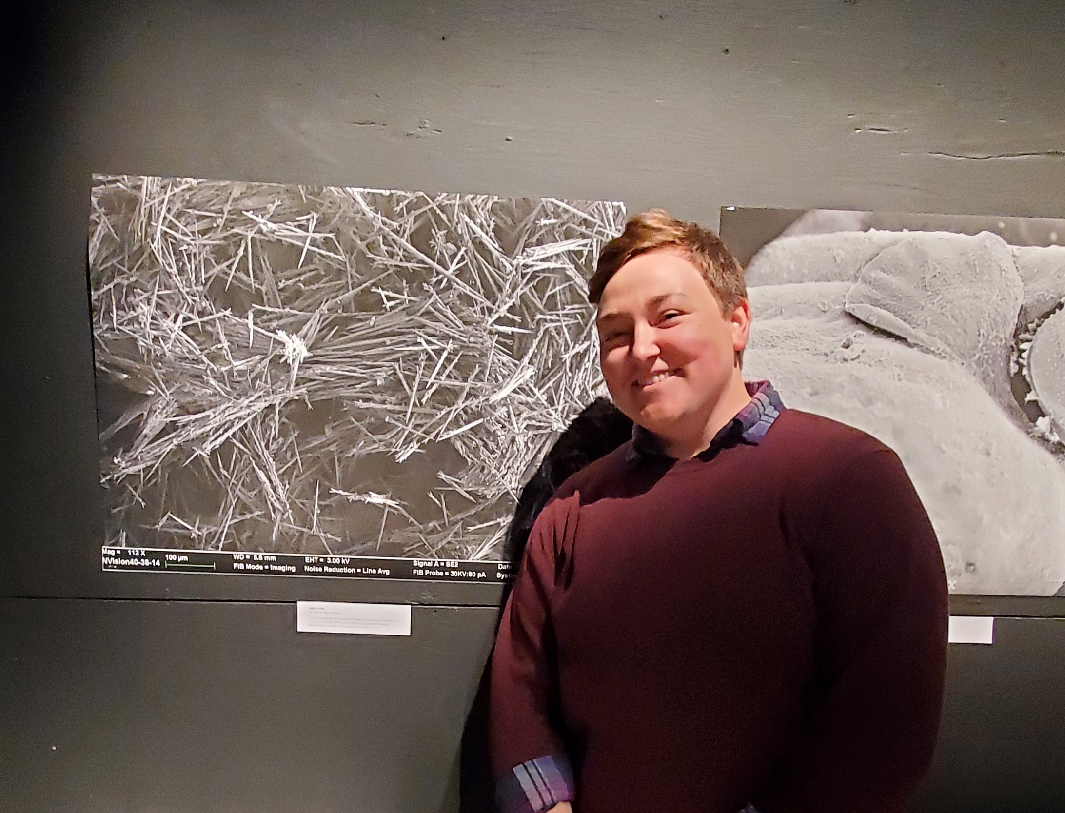 School of Biology and Ecology student Sadia Crosby stands to the right of a large print. The print is a highly-magnified image of browntail moth hairs.