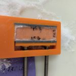 The completed Ice Vice, an orange plastic housing with an interior wall that can be adjusted by screws on the vice's exterior. The vice contains a small sample prepared for imaging, surrounded by ice shavings