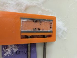 The completed Ice Vice, an orange plastic housing with an interior wall that can be adjusted by screws on the vice's exterior. The vice contains a small sample prepared for imaging, surrounded by ice shavings